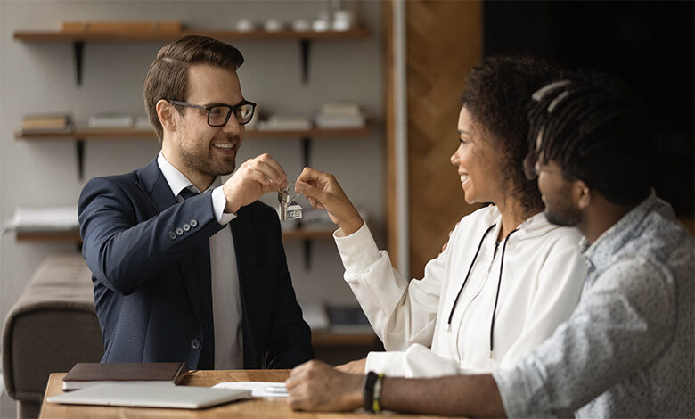 Real estate agent giving keys from new bought house own apartment to young excited couple